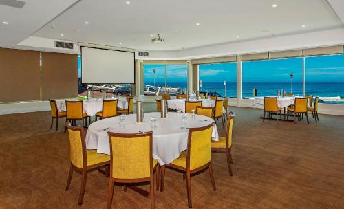 a dining room with tables and chairs and the ocean at Noah's On the Beach in Newcastle