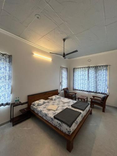 1 dormitorio con 1 cama, 2 sillas y ventanas en Iniyan Nestle, en Yercaud
