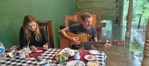 a man playing a guitar next to a woman at a table at Peacock Lake Villa in Habarana