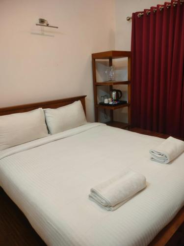 a bedroom with a white bed with a red curtain at Blissfull Meadows in Ooty