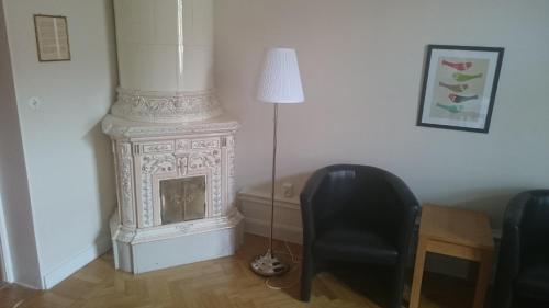 a white fireplace in a room with a chair and a lamp at First Hotel City Eskilstuna in Eskilstuna