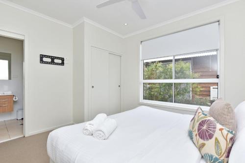 a white bedroom with a bed and a large window at Beach Escape at Caves Beach Villas in Caves Beach