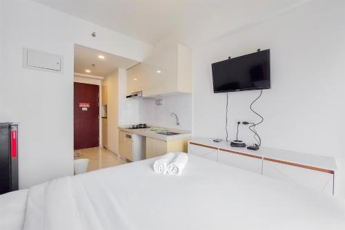 a white bedroom with a bed and a tv on the wall at Cozy Style Studio Room at High Floor Sky House BSD Apartment By Travelio in Tangerang