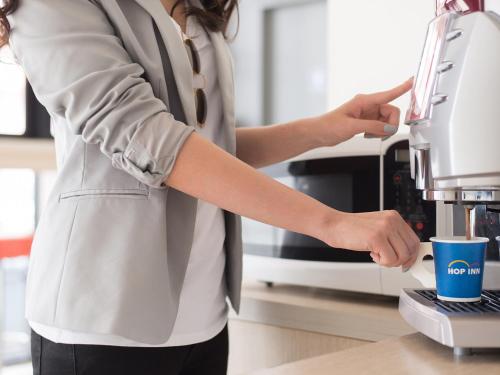 a woman standing in a kitchen using a coffee machine at HOP INN Khon Kaen Srichan Road Building B in Khon Kaen
