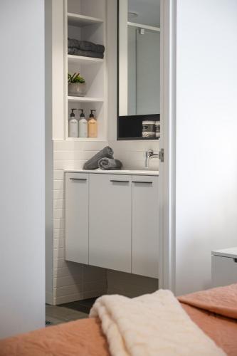 a white bathroom with a sink and a mirror at Luxe Flemington Cityscape Racecourse views Pool Gym Parking in Melbourne