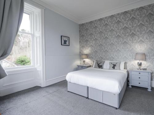 a white bedroom with a bed and a window at Glenspey in Kingussie