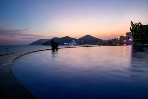 a couple sitting on the beach near the ocean at sunset at Harman Resort Hotel Sanya in Sanya