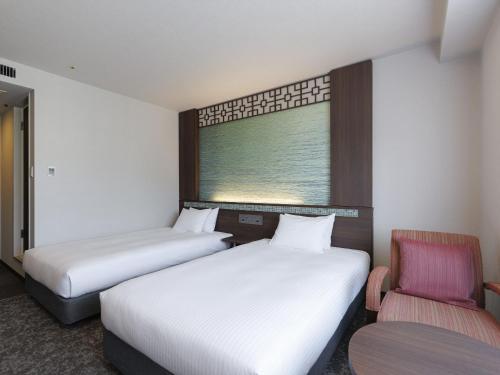 two beds in a room with a window and a chair at JR Kyushu Hotel Nagasaki in Nagasaki