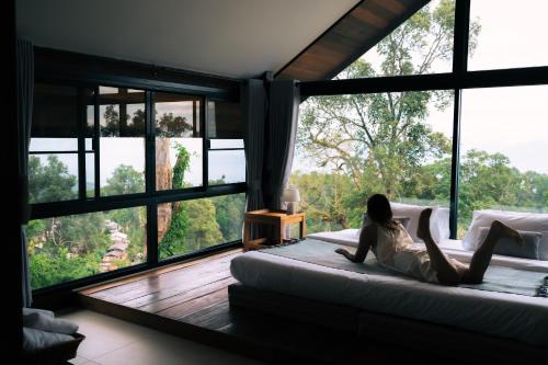 a woman laying on a bed in a room with large windows at Baan Nhuer Mek บ้านเหนือเมฆ Coffee and Desk on the Cloud in Ban Pang Klang