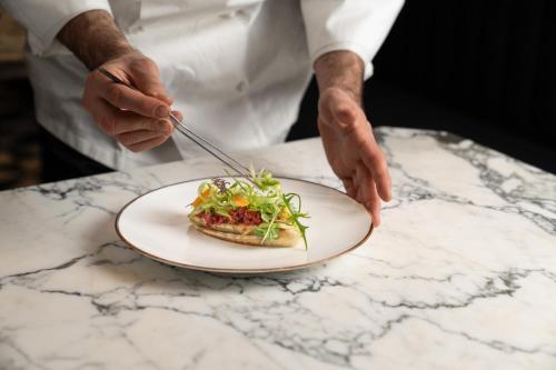 a chef is holding a plate of food on a table at The Goethe Hotel - Small Luxury Hotels of the World in Rome