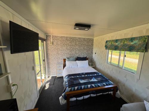 a bedroom with a bed and a flat screen tv at Cosy Cabin Retreat in Makirikiri