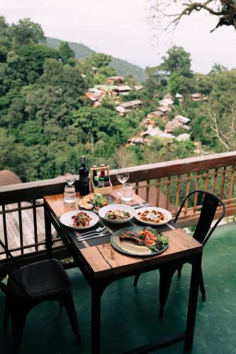 a wooden table with plates of food on a balcony at Baan Nhuer Mek บ้านเหนือเมฆ Coffee and Desk on the Cloud in Ban Pang Klang