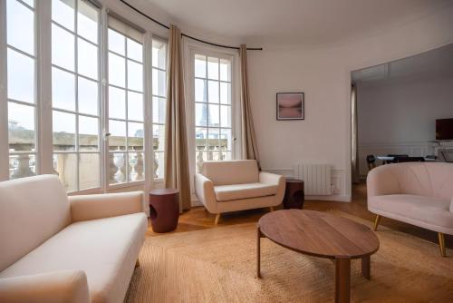 Elle comprend un salon doté d'un mobilier blanc et de grandes fenêtres. dans l'établissement TBS 325 - Superb apartment with Eiffel Tower view, à Paris