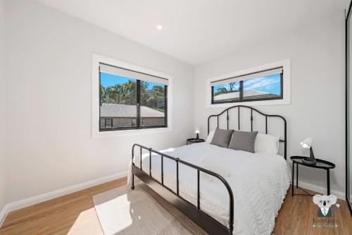 a white bedroom with a bed and two windows at KozyGuru | Cobbitty | Brand New Stylish 4BR House in Cobbitty