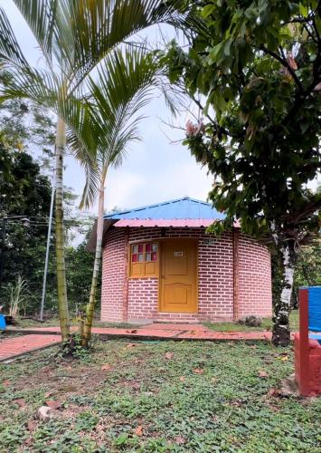 a red brick house with a yellow door and two palm trees at Hotel Centro vacacional El Cielo in Rivera