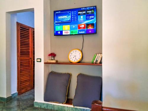 a tv on a wall with two chairs and a clock at Modern Girasoli Suites 03 in Malindi