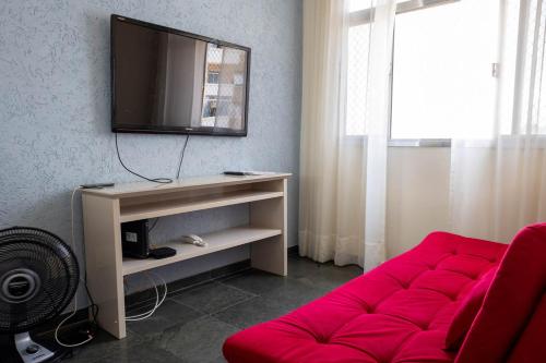 Una sala de estar con un sofá rojo y un televisor de pantalla plana. en Otimo apartamento a 200m do mar com WiFi, en Campo Grande