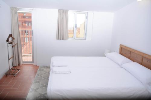 a white bedroom with two beds and a window at Pigal in Tarragona