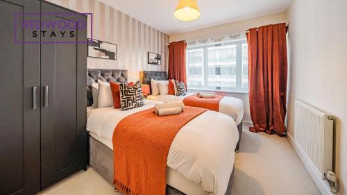 two beds in a bedroom with orange curtains at Premium Serviced Apartment in Basingstoke Town Centre, Free Parking By Redwood Stays in Basingstoke