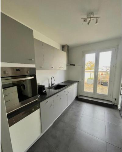 une cuisine avec des placards blancs et une grande fenêtre dans l'établissement LAGRIVE - Appartement avec balcon, à Reims