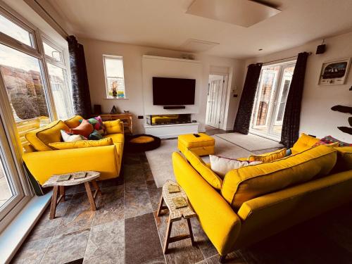 a living room with two yellow couches and a tv at 2-Bed Coastal Haven with Private Hot Tub in Lowestoft