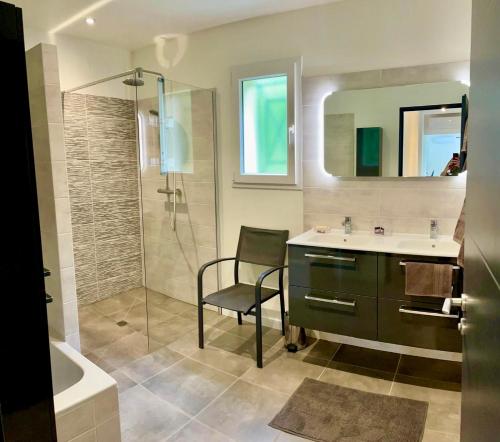 a bathroom with a sink and a shower and a chair at Le chant du Gave- Maison neuve lumineuse avec piscine- Rivière en contrebas du jardin in Sauveterre