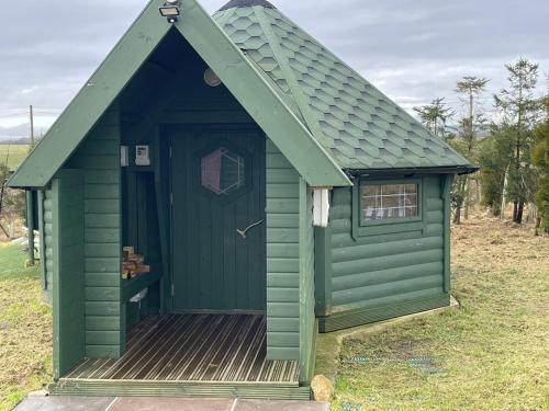 a green outhouse with a wooden deck in a field at Holly Tree Glamping Cabins in Wigglesworth