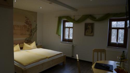 a bedroom with a bed and a table and two windows at Pension Mühlrad in Herbsleben