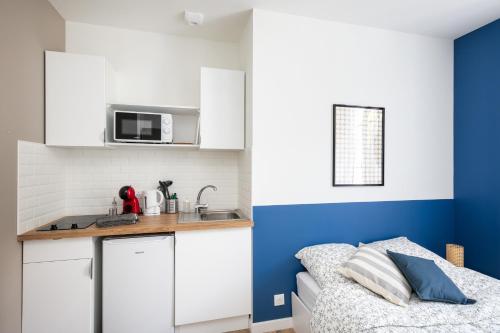 Elle comprend une petite cuisine avec des placards blancs et un mur bleu. dans l'établissement Ribine, à Brest