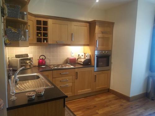 cocina con armarios de madera, fregadero y fogones en Lodge on Grounds of Ballykisteen Golf Resort, en Tipperary
