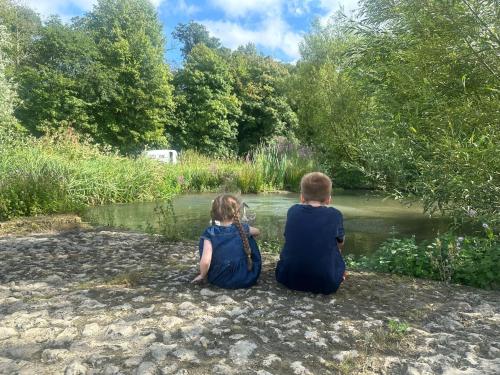 a boy and a girl sitting on the shore of a river at Farm woodland riverview cabin bbq firepit pet friendly in Hertford