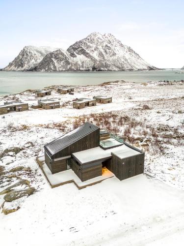 a house in a snowy field with mountains in the background at Hoda Cabin - Luxury lodge with jacuzzi and sauna in Lyngværet