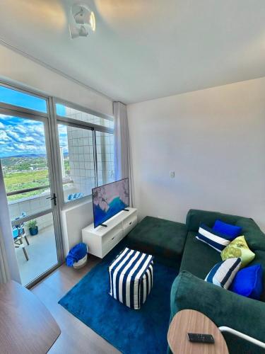 a living room with a green couch and a large window at Linda cobertura duplex com varanda no Vila da Serra in Nova Lima