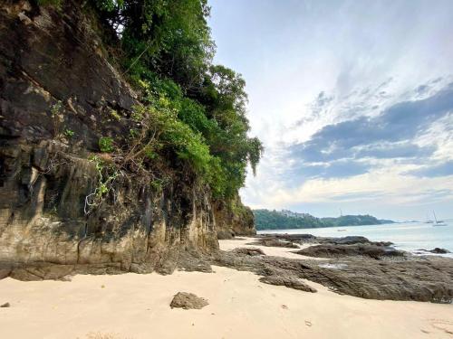 a sandy beach next to the ocean with a cliff at The Pixel Cap Panwa Sea front Condominium - By Lovly in Ban Ao Makham