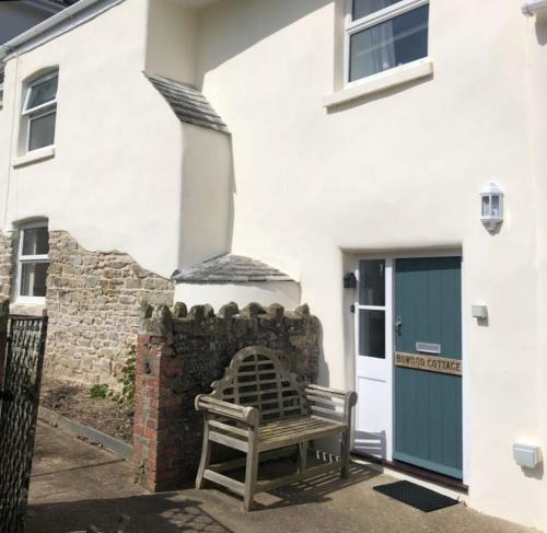 eine Holzbank vor einem weißen Gebäude in der Unterkunft Bowood Cottage in Abbotsham