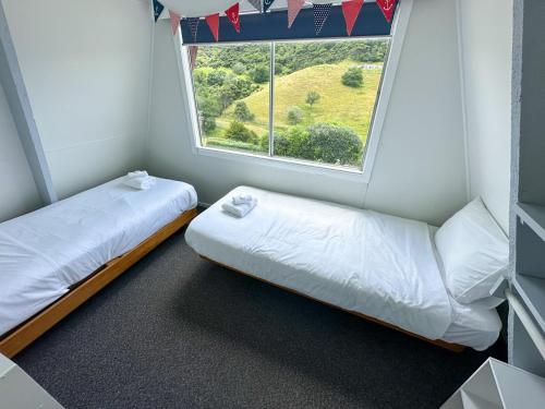 a small room with two beds and a window at Aroha A-Frames - Bush & Beach Retro Retreat in Coromandel Town