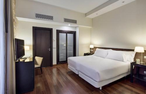 a bedroom with a large white bed and a television at Sercotel Puerta de la Catedral in Salamanca