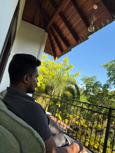 a man sitting on a balcony looking out the window at Gold Crown Residence in Dambulla