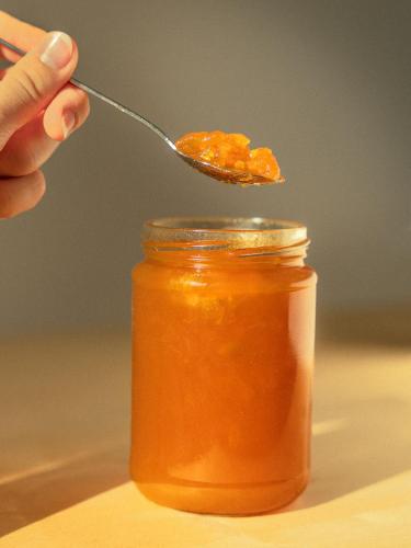 a hand holding a spoon with a jar of honey at Gästehaus Freitag das kleine Hotel in Sankt Georgen