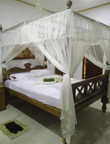 a bedroom with a canopy bed with white drapes at Chapel Home Stay in Ahungalla