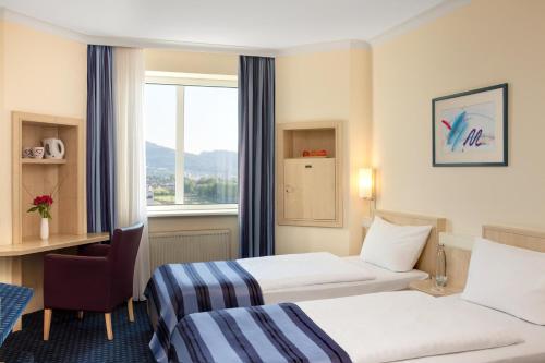a hotel room with two beds and a desk and a window at IntercityHotel Freiburg in Freiburg im Breisgau