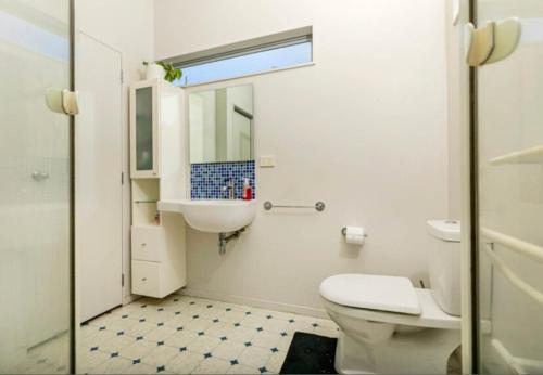 a white bathroom with a toilet and a sink at Cosy Bush Apartment in Auckland