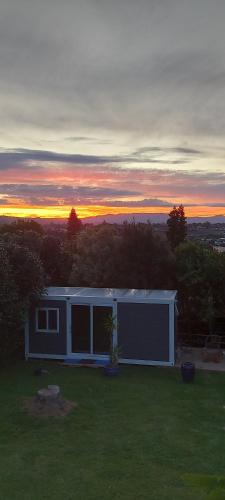 a house in a field with the sunset in the background at Haley's cabin in Tauranga