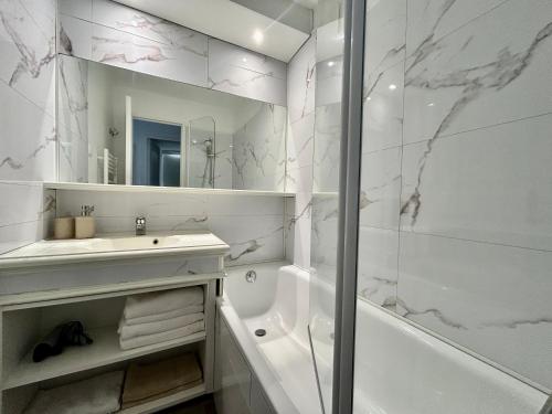 ein weißes Badezimmer mit einer Badewanne, einem Waschbecken und einem Spiegel in der Unterkunft Les Restanques vue mer Capucines 1057 in Grimaud