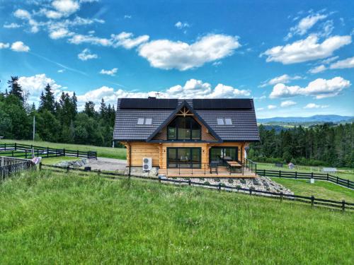 a log cabin with a black roof on a green field at LK Forest Villa luksusowe domy z basenem z jacuzzi, sauną, grotą solną, salą bilardową i ogrodem in Łapsze Niżne