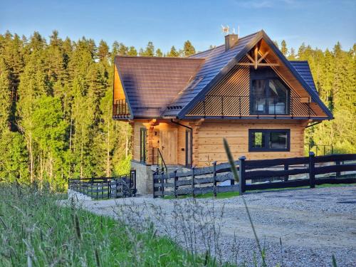 a wooden house with a fence in front of a forest at LK Forest Villa luksusowe domy z basenem z jacuzzi, sauną, grotą solną, salą bilardową i ogrodem in Łapsze Niżne