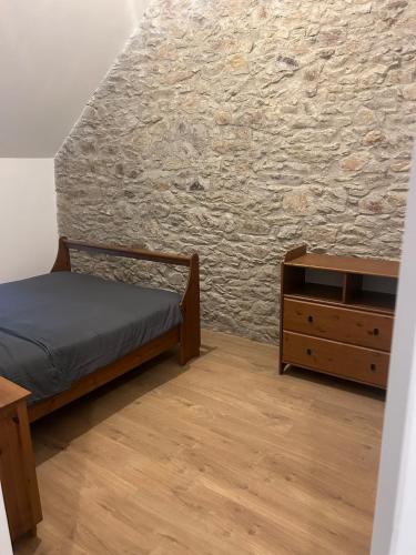 - une chambre avec un lit, une commode et un mur en pierre dans l'établissement Le domaine des mortiers appartement T2, à Saint-Étienne-de-Montluc