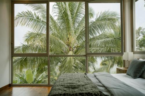 a bedroom with a large window with a palm tree outside at Trails, waterfalls & chill in private jungle lodge in Selemadeg