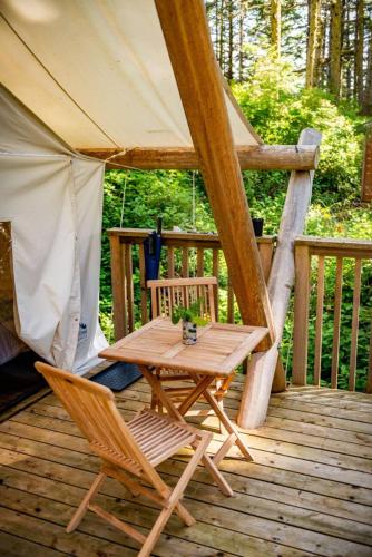 a wooden table and chairs on a deck with a tent at Haida Gwaii Glamping in Tlell