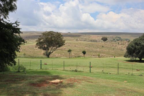 a fence in the middle of a field with trees at Field and Stream in Dullstroom